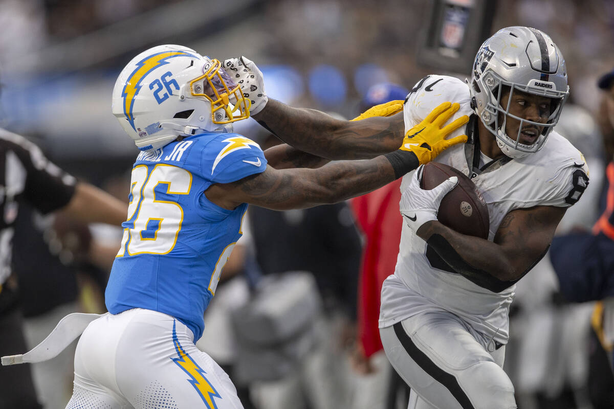 Raiders running back Josh Jacobs (8) throws a stiff arm against Los Angeles Chargers cornerback ...