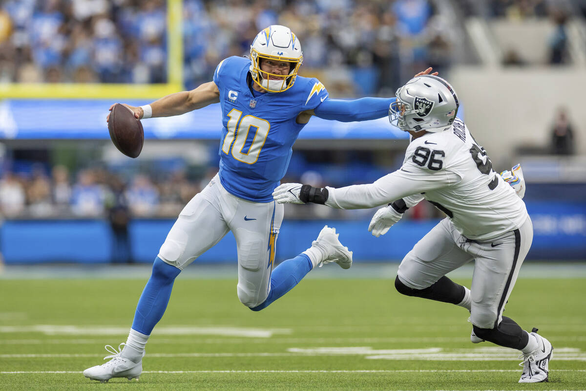 Los Angeles Chargers quarterback Justin Herbert (12) scrambles and stiff arms Las Vegas Raiders ...