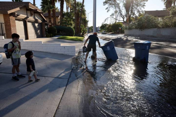 A resident retrieves their trash bins as Las Vegas Valley Water District employees work on a wa ...