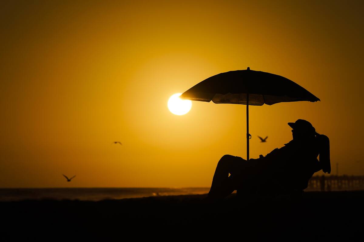FILE - A person rests under an umbrella as the sun sets, Sept. 12, 2023, in Newport Beach, Cali ...