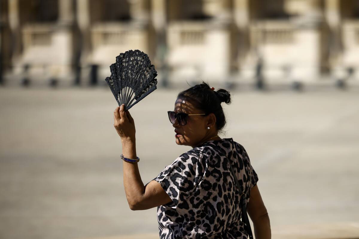 FILE - A woman uses a fan in the courtyard of the Louvre museum, Sept. 7, 2023, in Paris. After ...