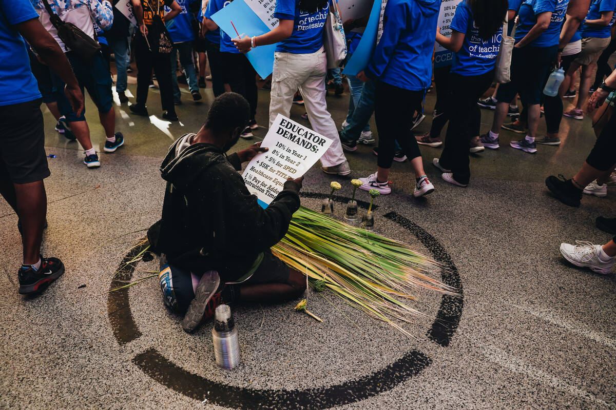 A busker reads a protest sign as demonstrators walk by in support of the Clark County Education ...