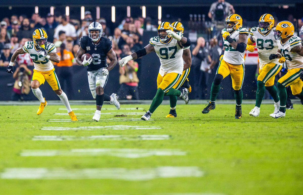 Raiders running back Josh Jacobs (8) runs away from a host of Green Bay Packers defenders durin ...