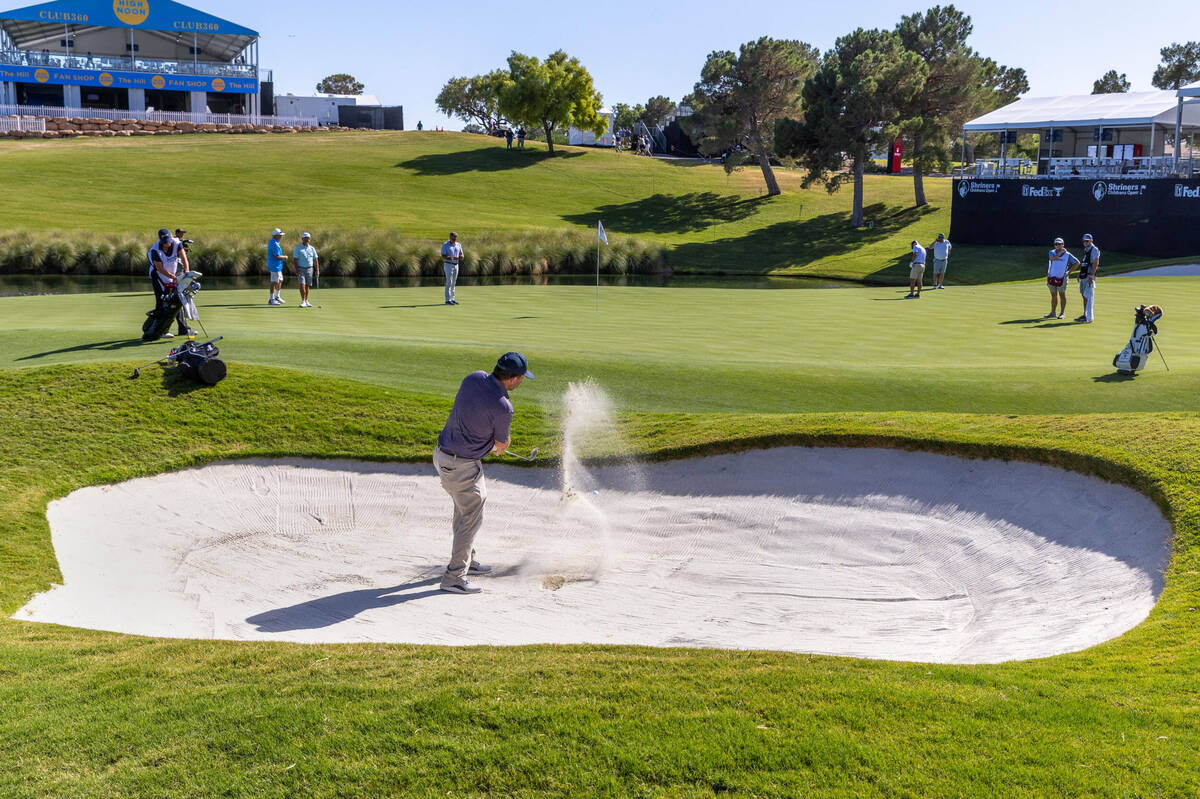 A golfer hits out of the sand onto the green at hole 18 during the Pro Am before the Shriners C ...