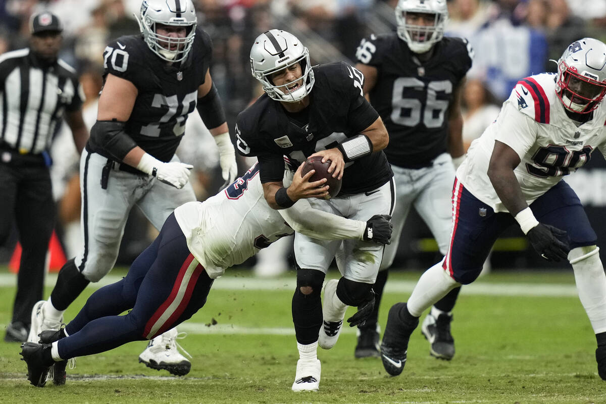 Las Vegas Raiders quarterback Jimmy Garoppolo, center, is hauled down by New England Patriots l ...