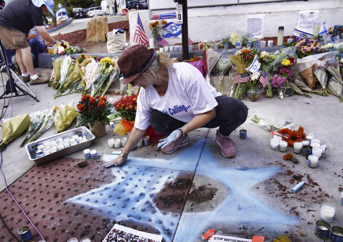 Elena Colombo chalks a Star of David amongst flowers and candles left at a makeshift shrine pla ...
