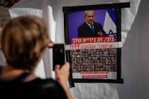A woman takes a photo of a poster showing Israelis held captive in Gaza plastered underneath a ...