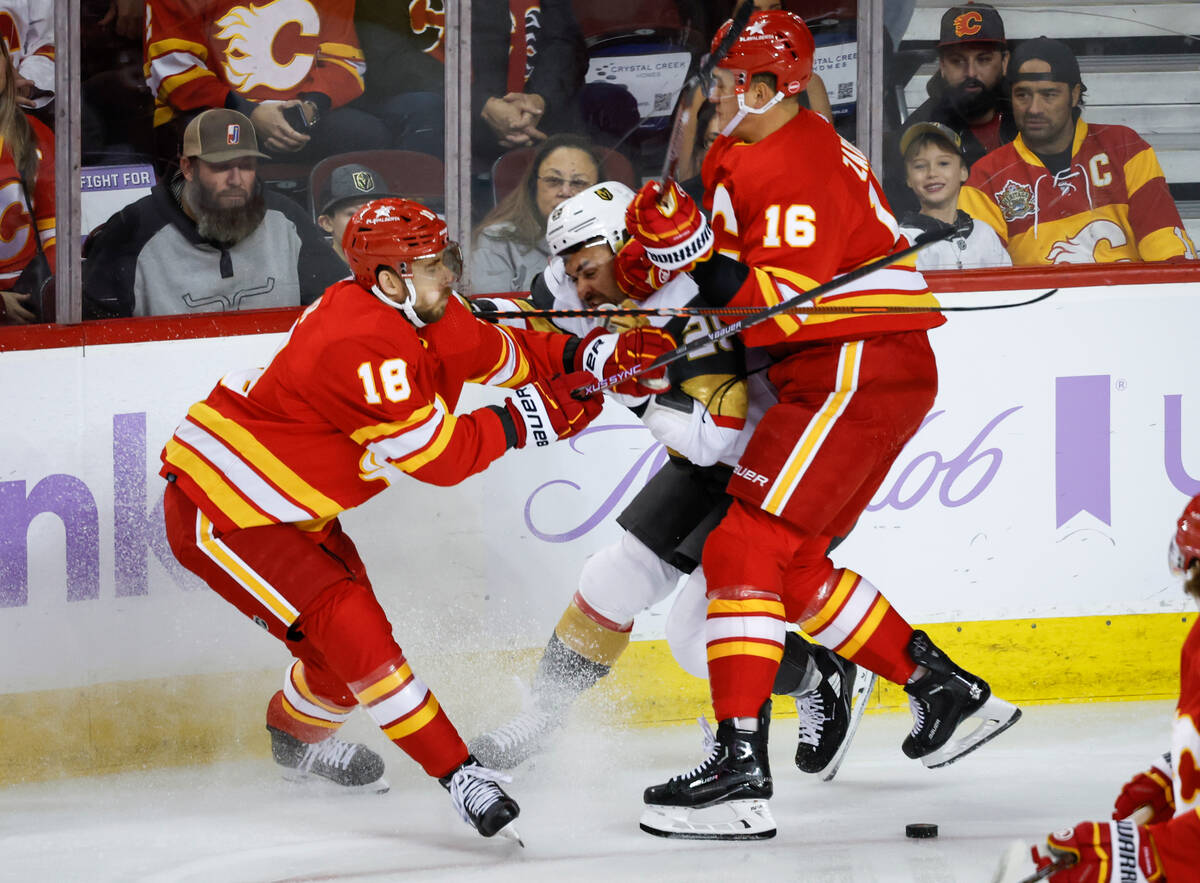 Vegas Golden Knights forward William Carrier, center, is checked by Calgary Flames forward A.J. ...
