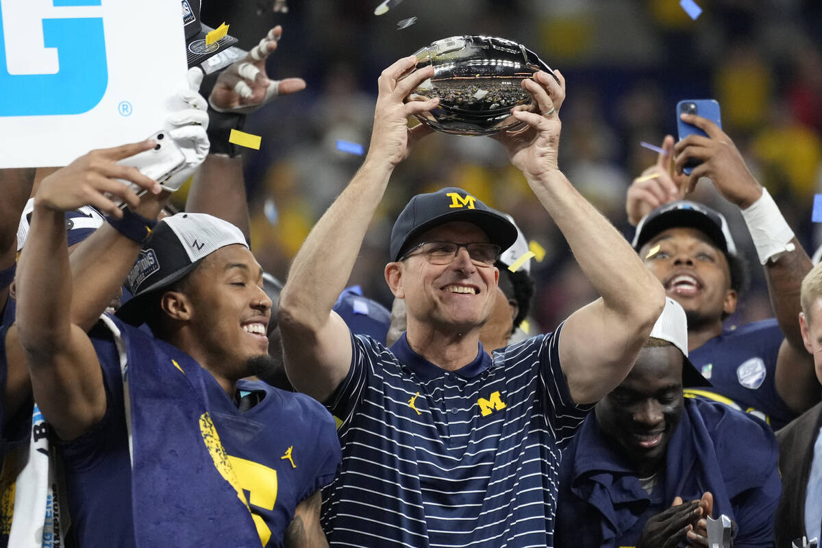 FILE - Michigan head coach Jim Harbaugh holds the trophy as he celebrates with his team after d ...