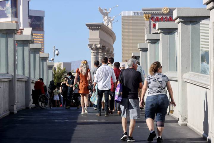 People walk on the pedestrian bridge between the Bellagio and Caesars Palace on the Strip in La ...