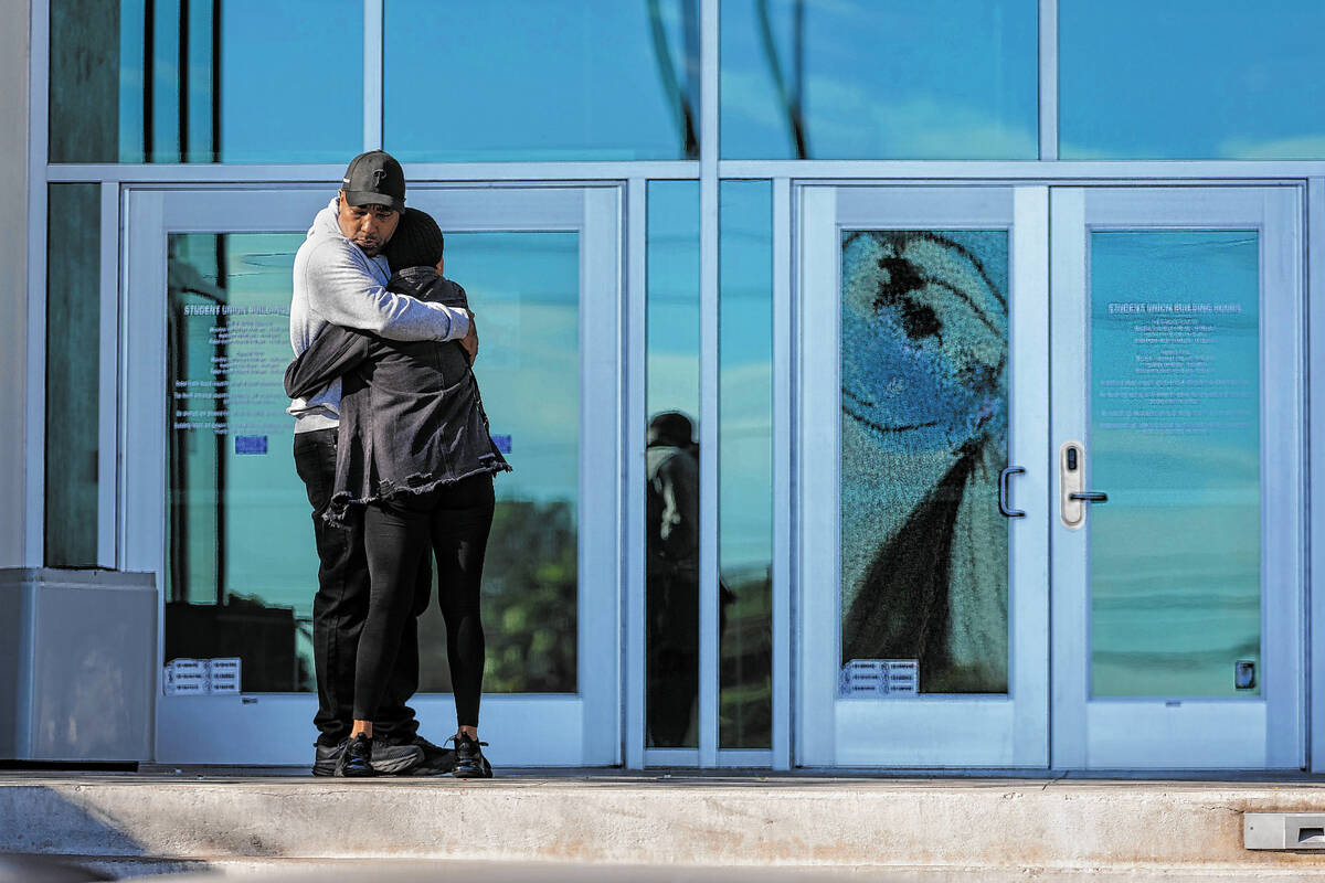 Two people hug near a shattered front door glass panel at the Student Union following the shoot ...