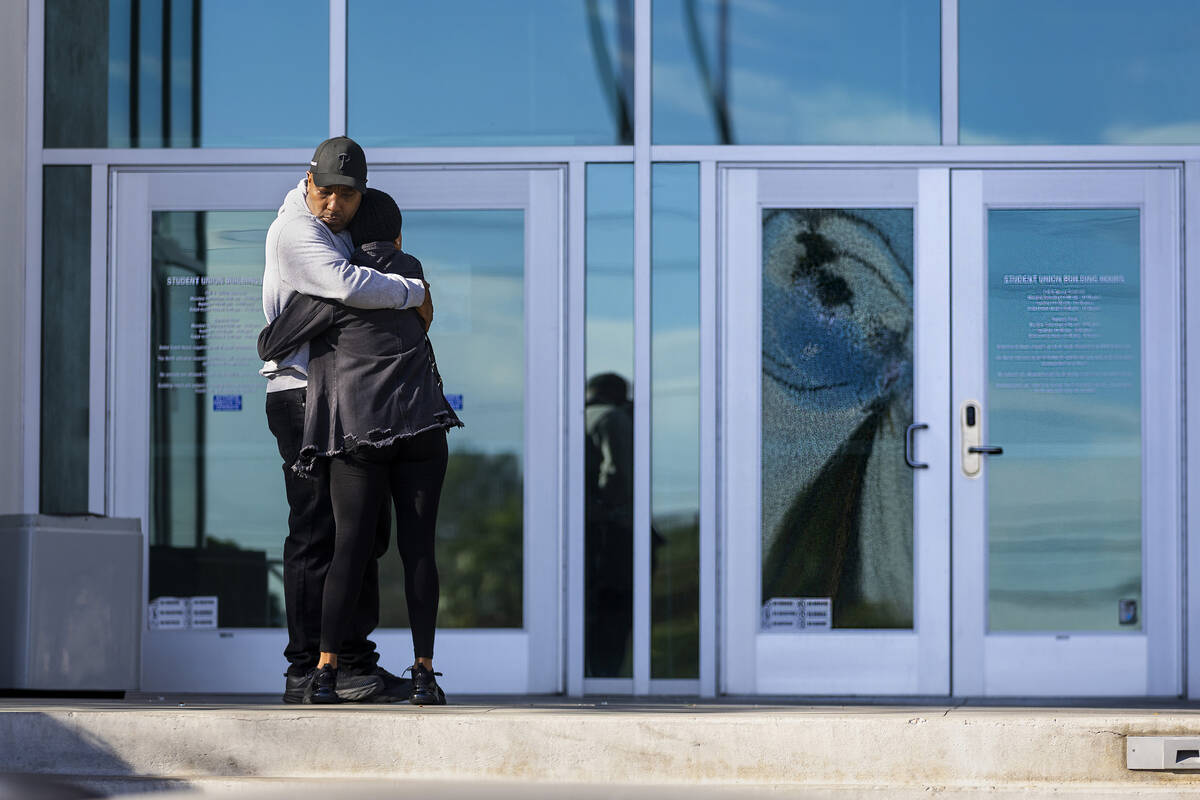 Two people hug near a shattered front door glass panel at the Student Union following the shoot ...