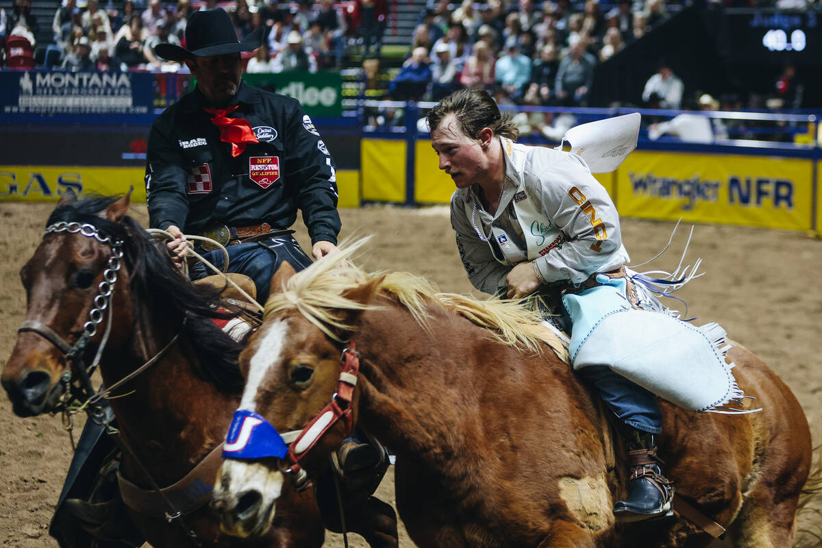A pickup rider helps Keenan Hayes off of Lil Red Hawk during round one of bareback riding NFR a ...