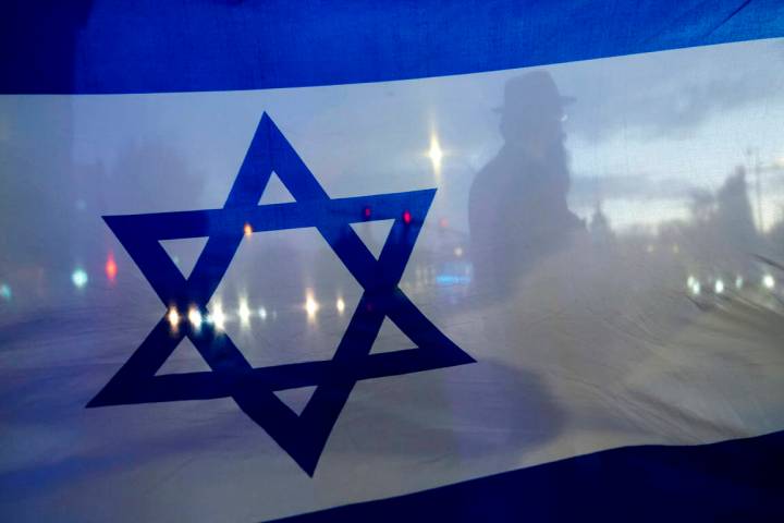 A demonstrator is silhouetted behind a flag of Israel during a rally in support of Israel on Oc ...