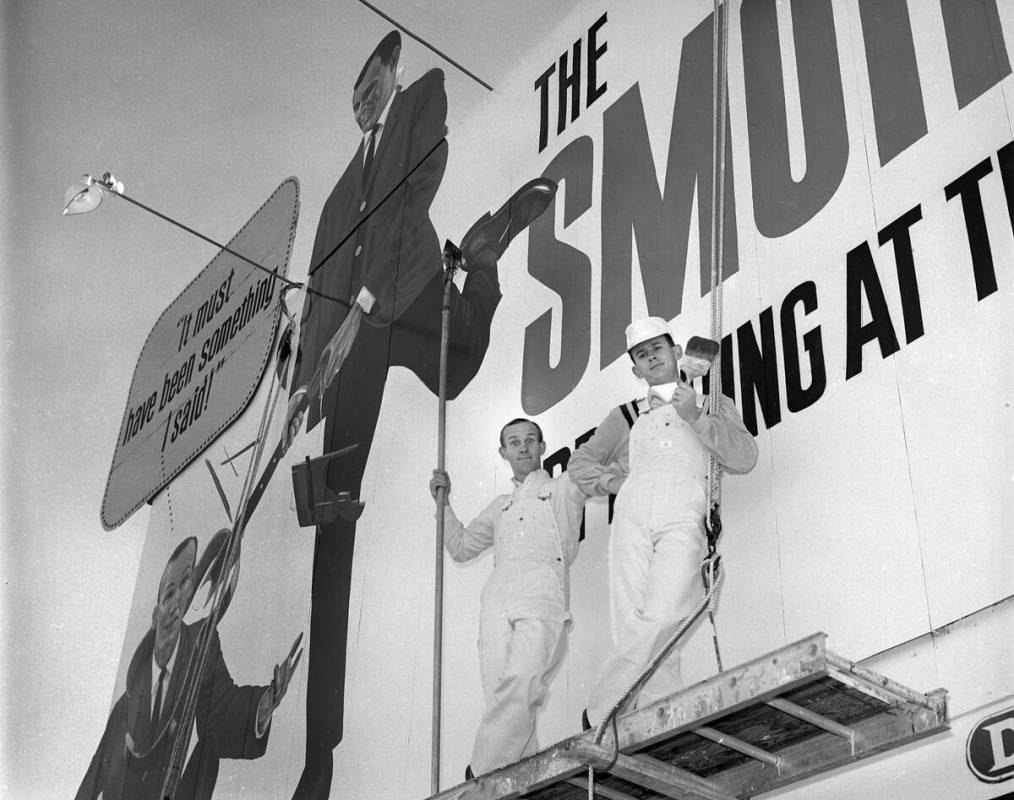 Tom, à esquerda, e Dick Smothers posam como pintores ao lado de um outdoor em um anúncio na Las Vegas Strip...