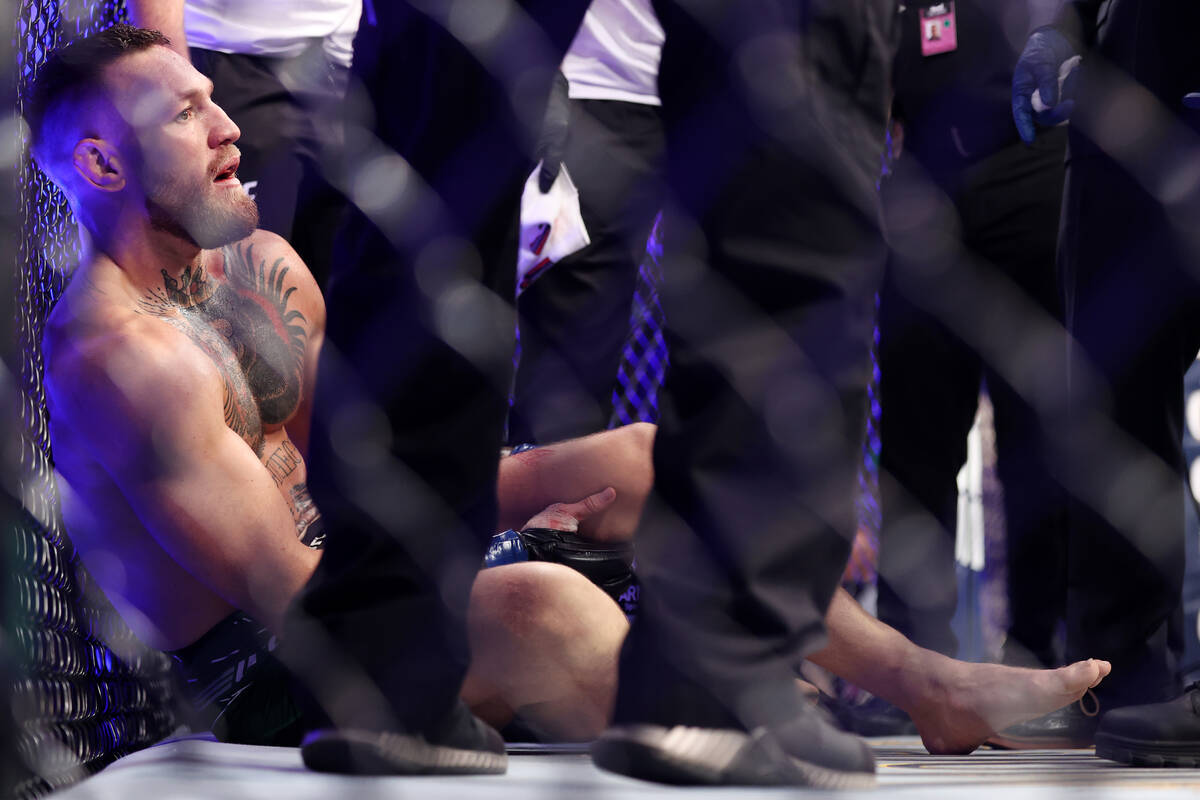 Conor McGregor receives assistance after hurting his foot in the first round of a lightweight b ...