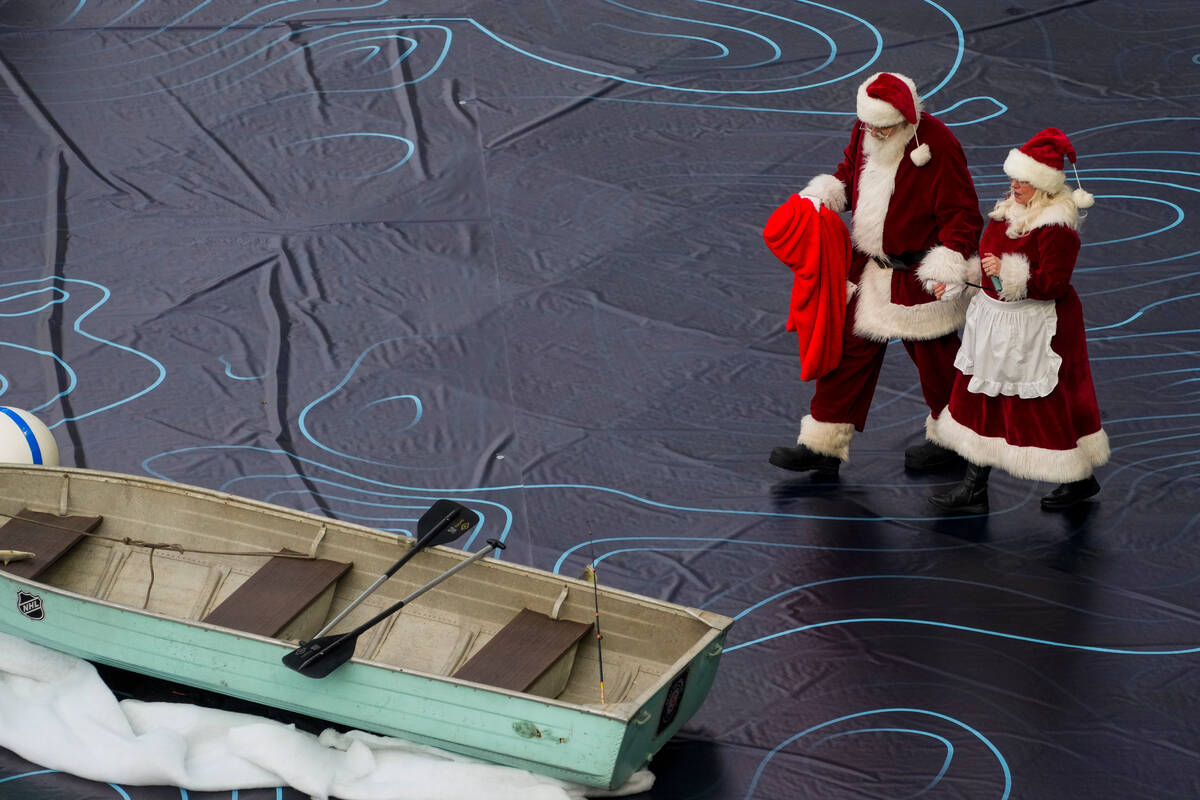 People dressed as Santa Claus and Mrs. Claus walk towards a rowboat in the outfield during the ...