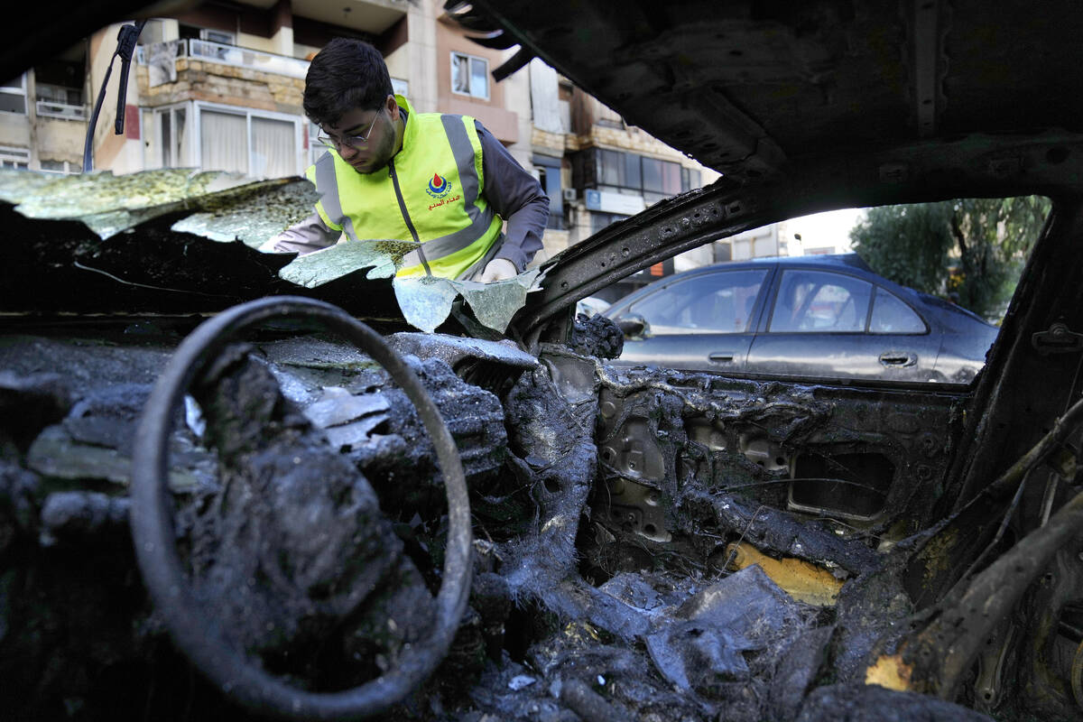 A Hezbollah Civil defense worker searches for body remains on a burned car, near an apartment b ...