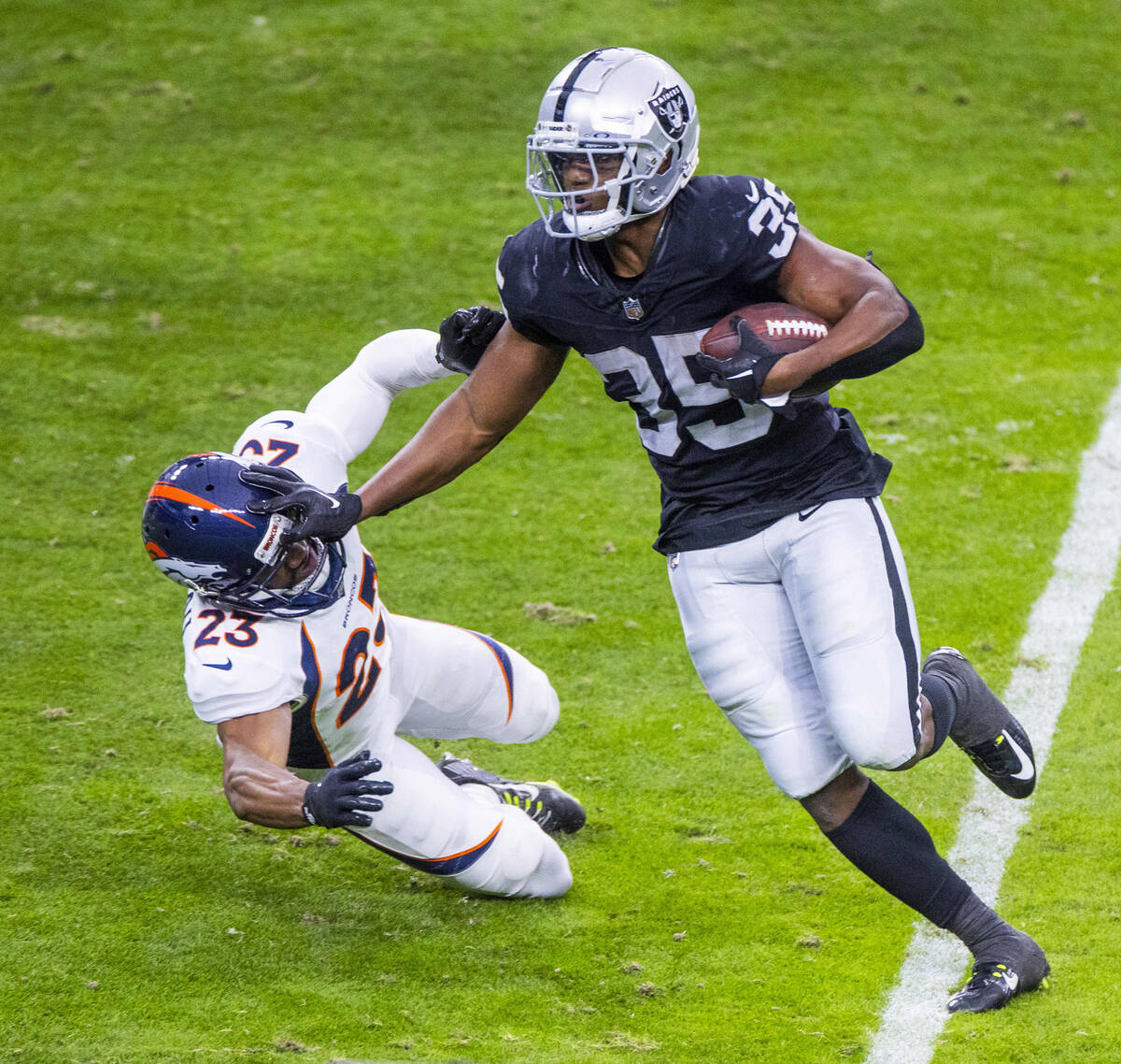 Raiders running back Zamir White (35) stiff arms Denver Broncos cornerback Fabian Moreau (23) o ...