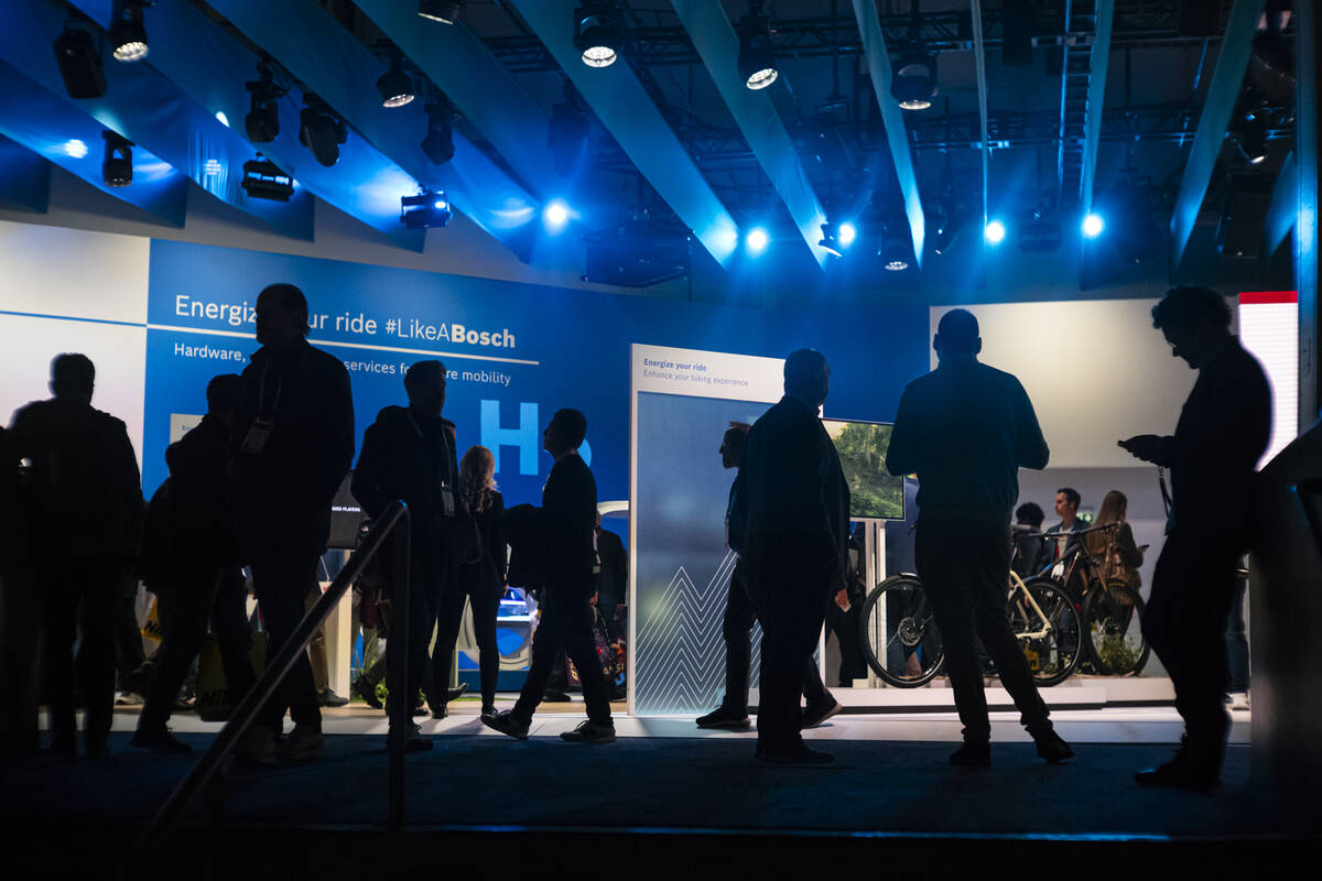 Attendees are silhouetted against the Bosch booth during the first day of CES at the Las Vegas ...