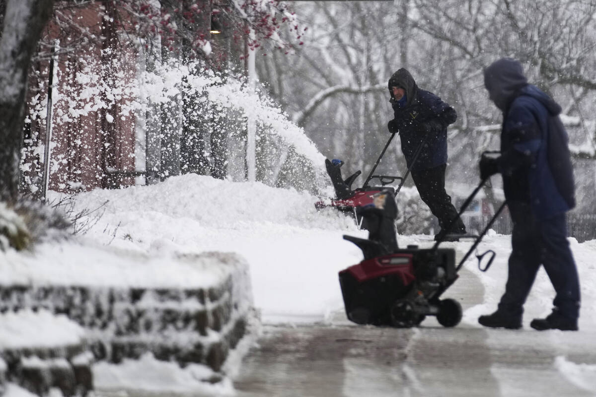 People clean a path from snow in front of a school in Wheeling, Ill., Friday, Jan. 12, 2024. (A ...