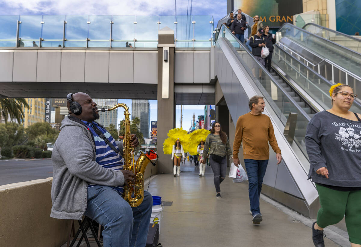 A saxophonist plays near the pedestrian bridge leading to the MGM as others walk by on Wednesda ...