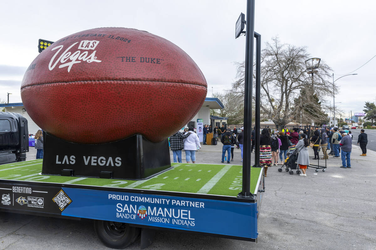 A small crowd gathers about the giant football during the first of Super Bowl "Green Week& ...