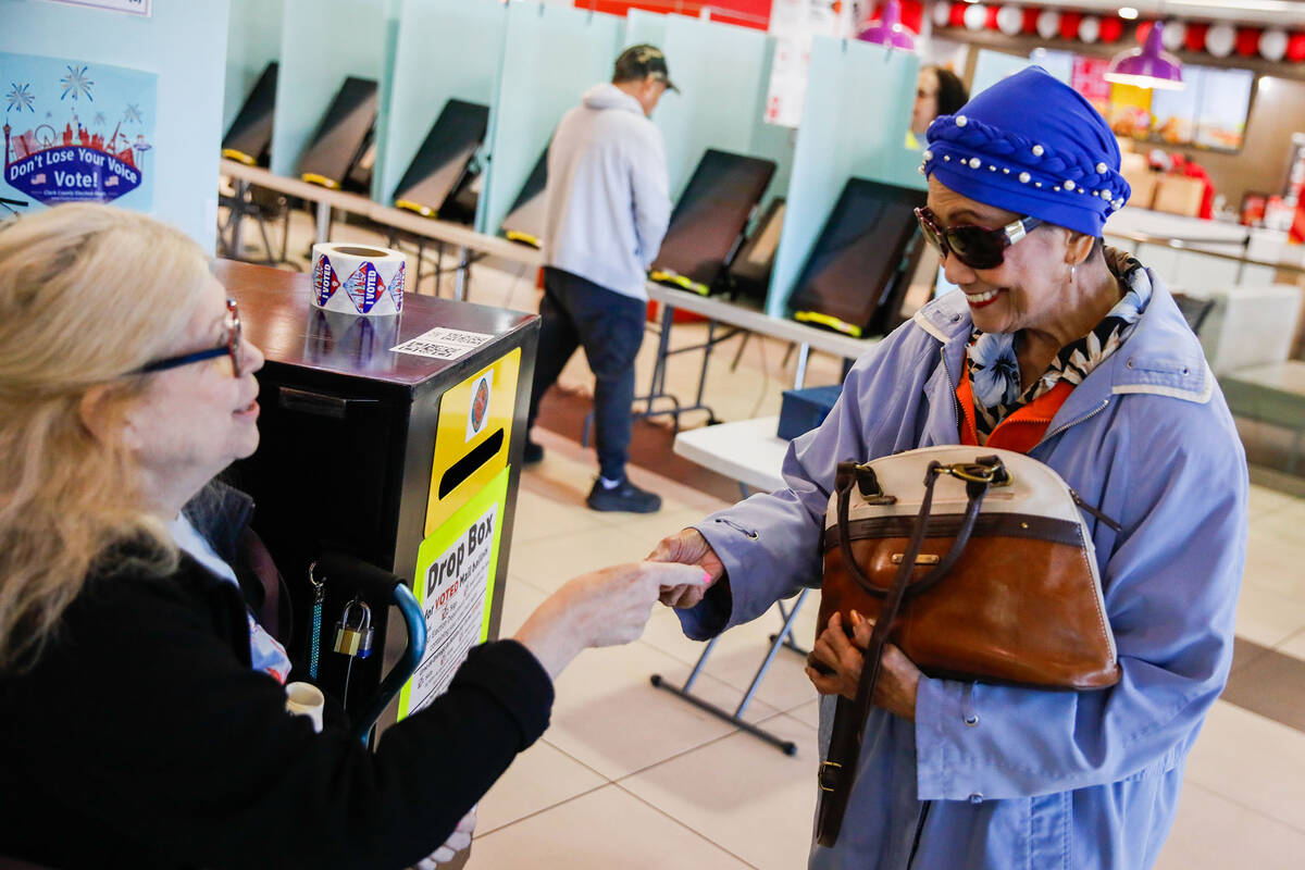 Dallas-Lee Brower, left, a poll worker, helps a voter drop off her ballot during early voting a ...