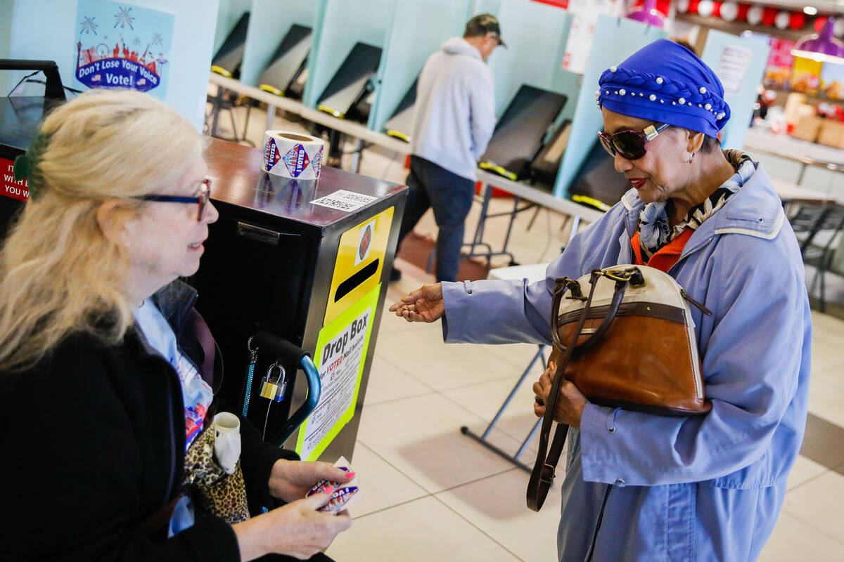 Dallas-Lee Brower, left, a poll worker, helps a voter drop off her ballot during early voting a ...