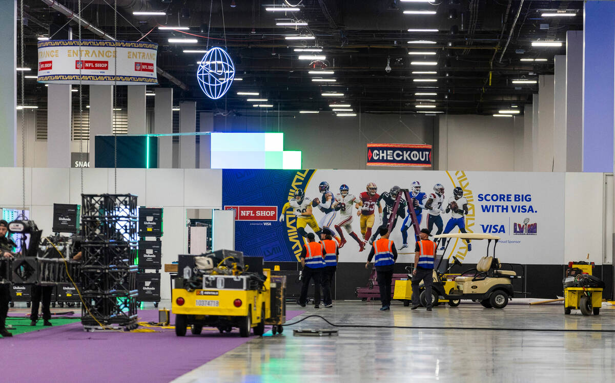Workers walk past the entrance to the NFL Shop as set up continues for the Super Bowl Experienc ...