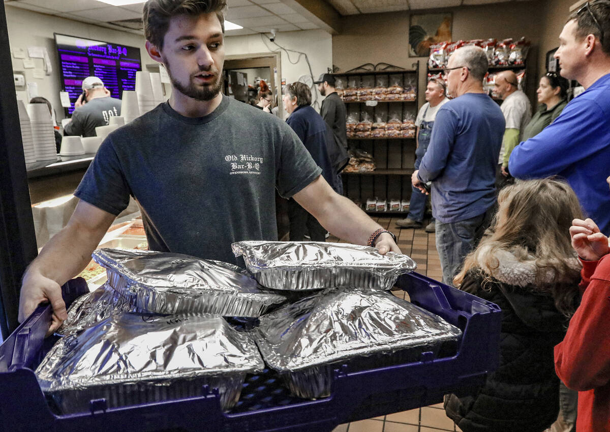 File - Old Hickory Bar-B-Que employee Tyler Reynolds carries a tray of sliced hams of the the r ...