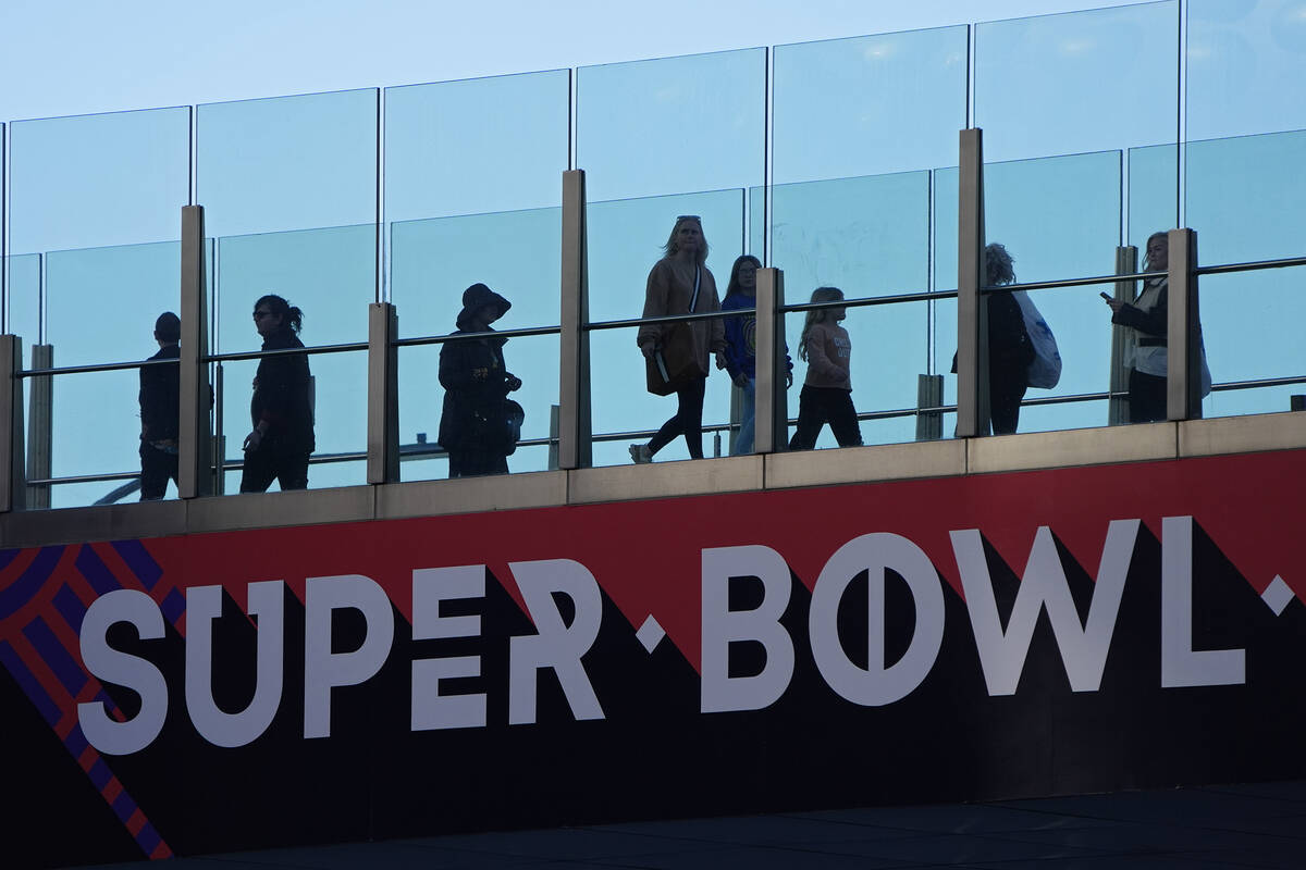 People walk across a pedestrian walkway along the Las Vegas Strip ahead of the Super Bowl 58 fo ...