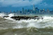 Waves crash over a breakwater in Alameda, Calif., with the San Francisco skyline in the backgro ...