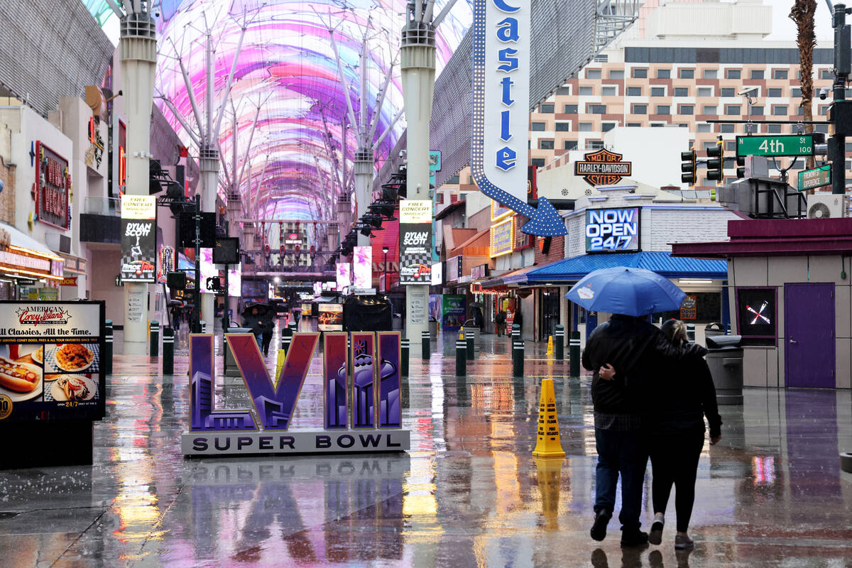 People walk in a light rain past a 2024 Super Bowl installation at the Fremont Street Experienc ...