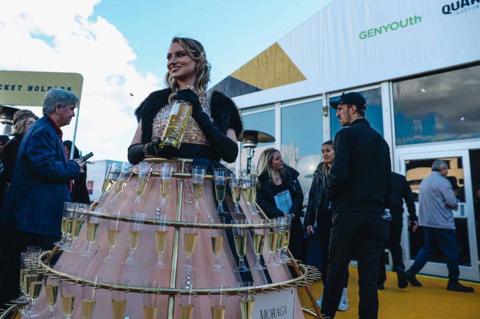 A woman wearing a dress holding wine glasses stands outside stands outside at the Taste of NFL ...