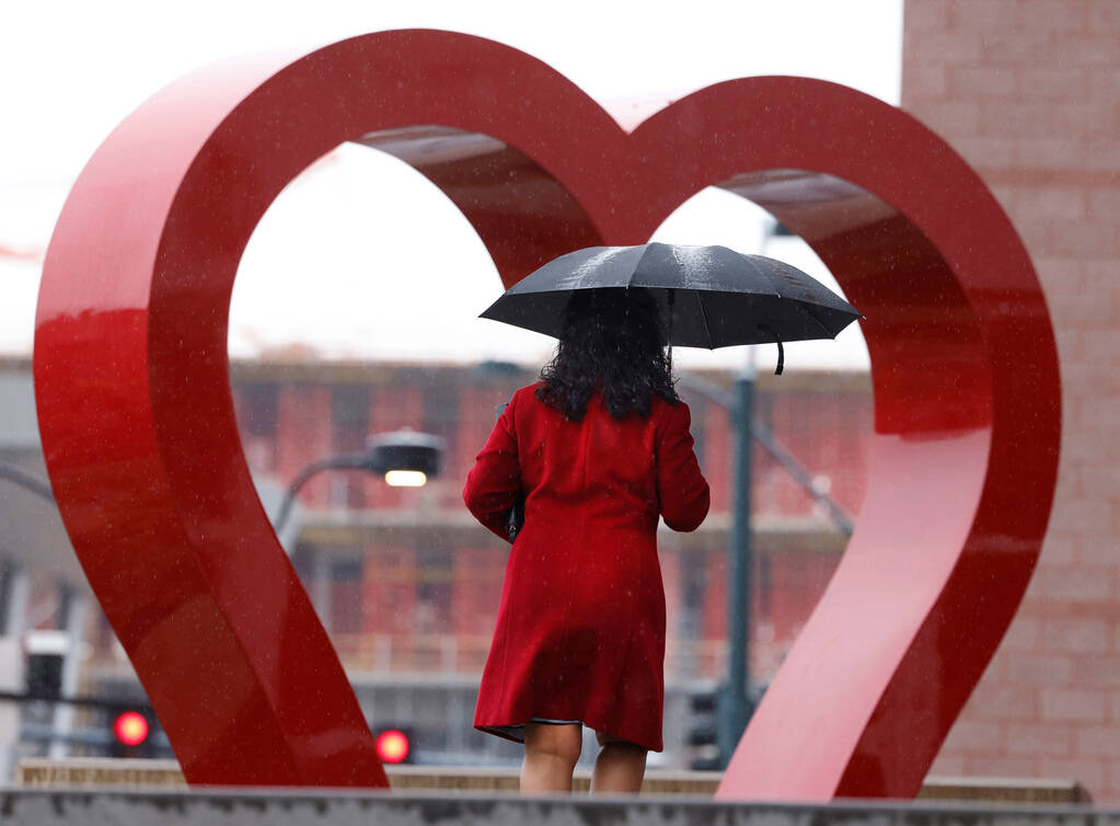 A pedestrian under un umbrella walks past a giant heart sculpture outside the Clark County Marr ...