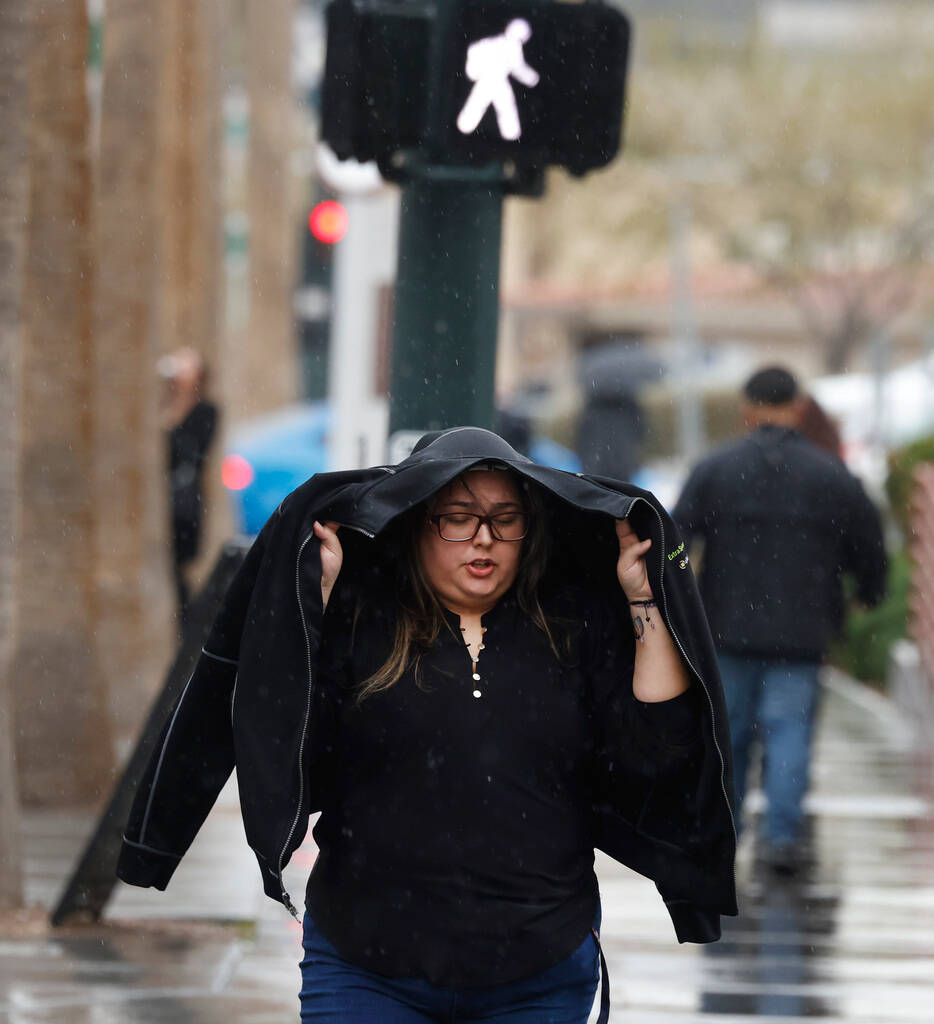 A pedestrian covers her head under her jacket as she walks along Third Street during a rainy mo ...
