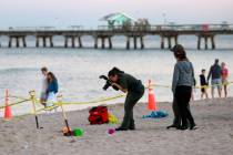 Investigators on the beach in Lauderdale-by-the-Sea take photos of the scene of a sand collapse ...