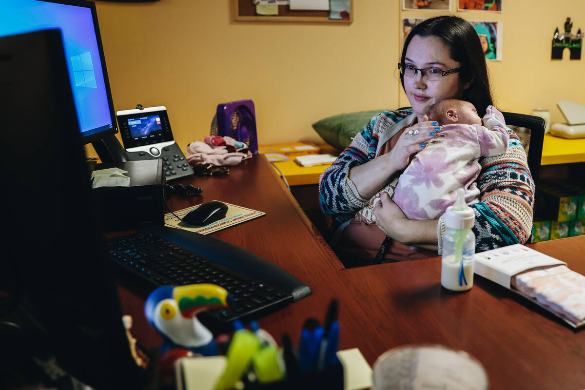 Katie Krikorian holds one of her foster children while checking her emails at her desk on the C ...