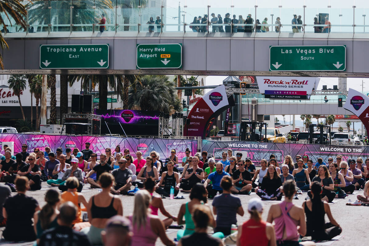 Pedestrians on the pedestrian bridge watch as people gather on the Strip to do yoga while it is ...