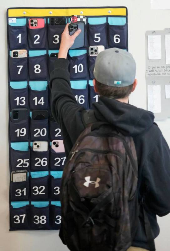 A ninth grader places his cellphone into a phone holder as he enters class at Delta High School ...