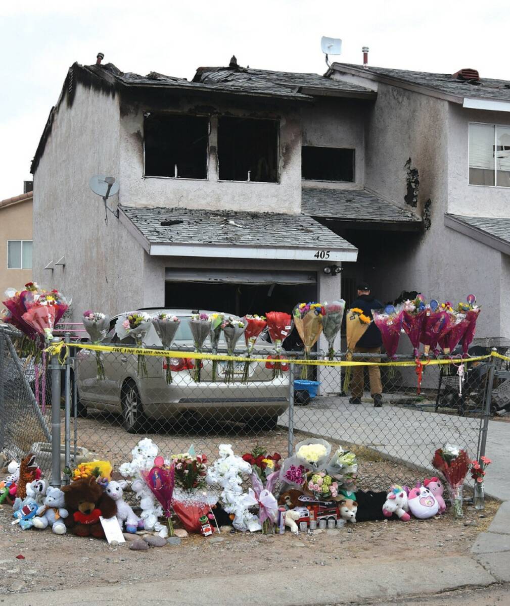 Flowers, stuffed animals and candles are placed on and along a chain-link fence in a makeshift ...