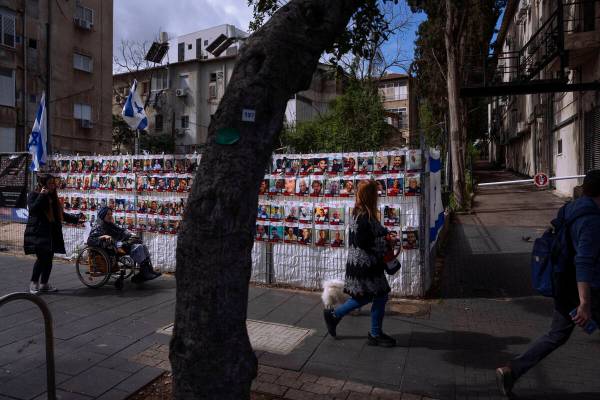 People pass by a fence with photographs of Israelis who are being held hostage in the Gaza Stri ...