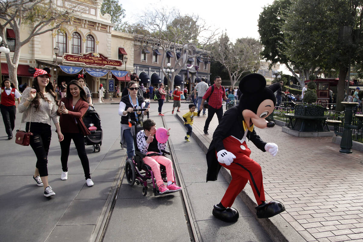 Visitors follow Mickey Mouse for photos at Disneyland, Jan. 22, 2015, in Anaheim, Calif. Disney ...