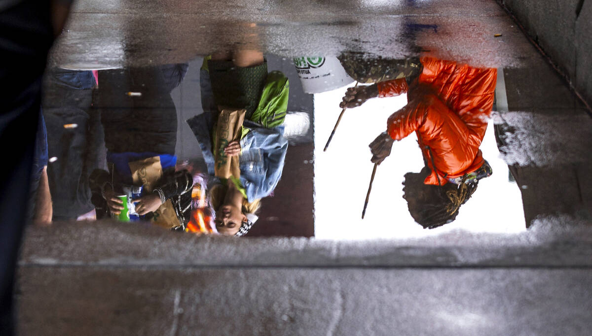 Joe Bob is reflected in a puddle as he drums on 5 gallons buckets as he entertains pedestrians ...