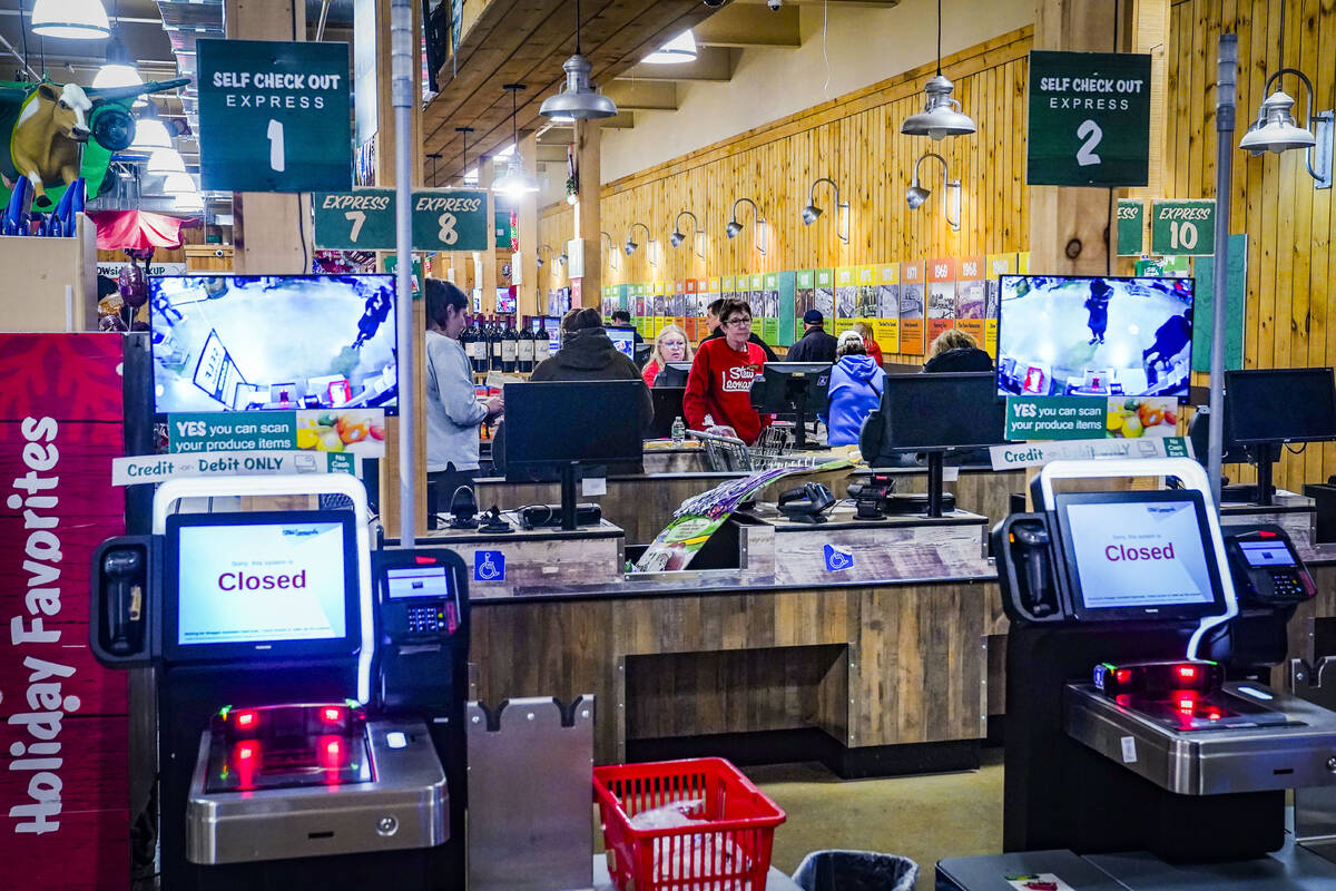 Customers checkout at registers with cashiers near a section of self-checkout kiosks at Stew Le ...