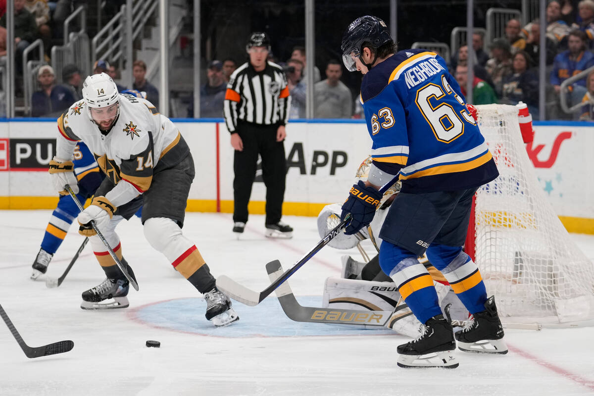 Vegas Golden Knights' Nicolas Hague (14) and St. Louis Blues' Jake Neighbours (63) watch the pu ...