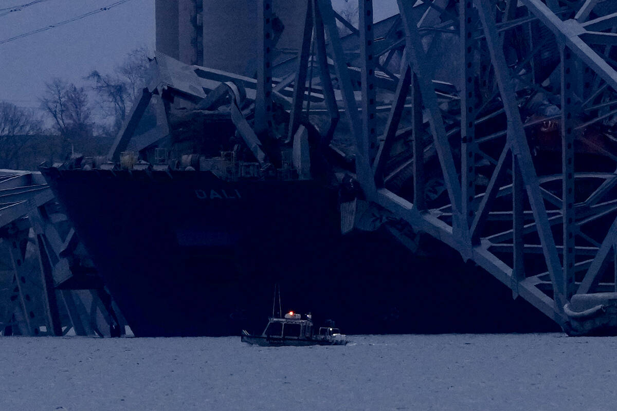 A container ship rests against wreckage of the Francis Scott Key Bridge as night falls on Tuesd ...