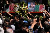 Iranian mourners try to touch the flag-draped coffins of Revolutionary Guard members killed in ...