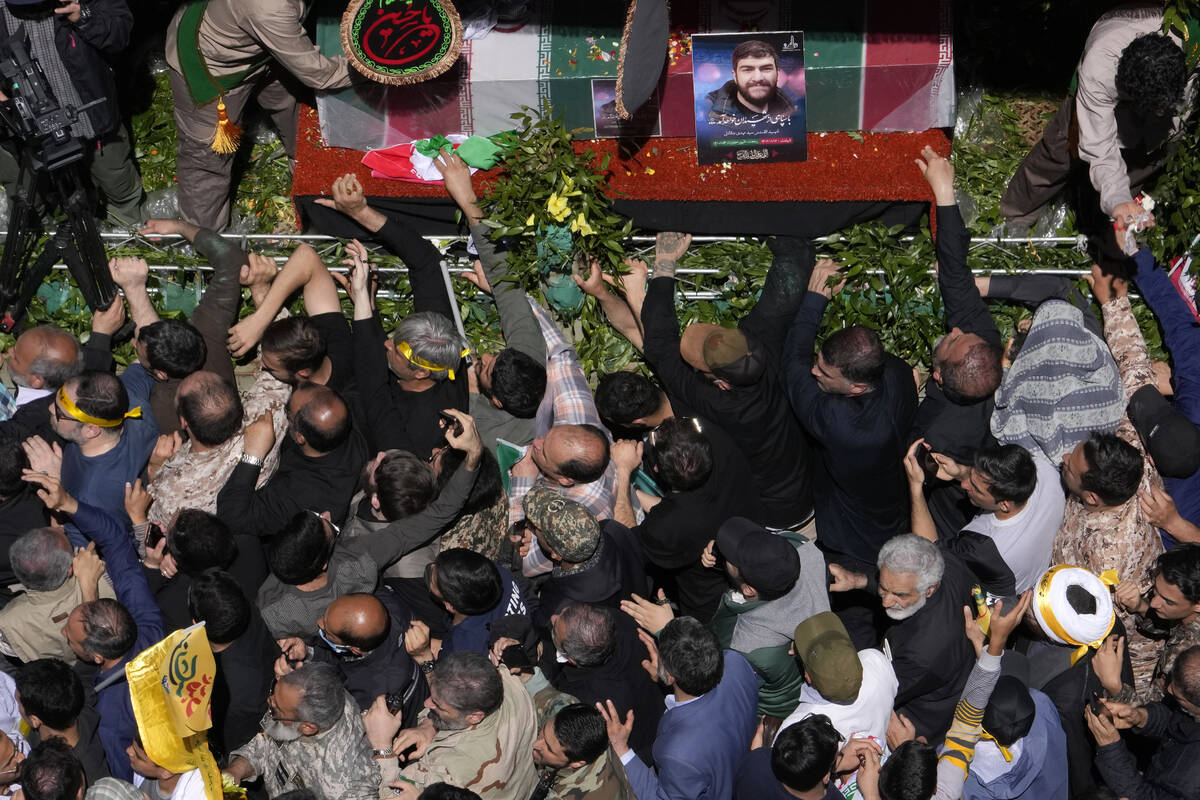 Iranian mourners try to touch the flag-draped coffins of Revolutionary Guard members killed in ...